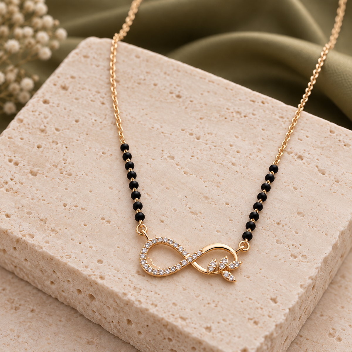 Ananta Mangalsutra infinity and leaf pendant viewed at an angle on ivory travertine