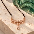 Angled view of Vanalika Mangalsutra on pale travertine with emerald glass