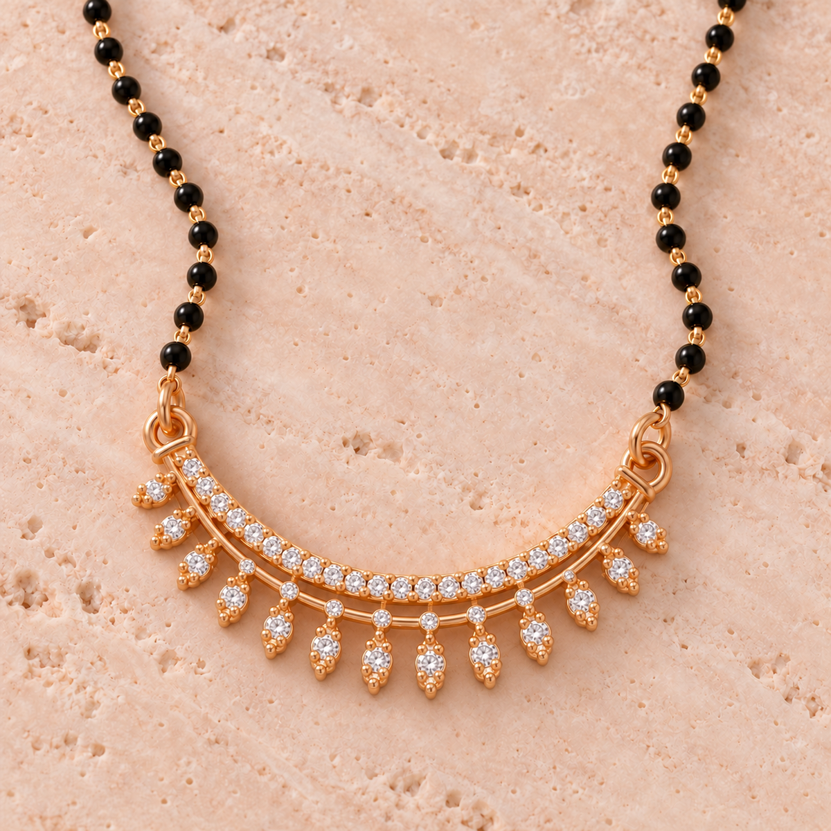 Close detail of Tarunika Mangalsutra curved clear accents and delicate fringe on blush travertine