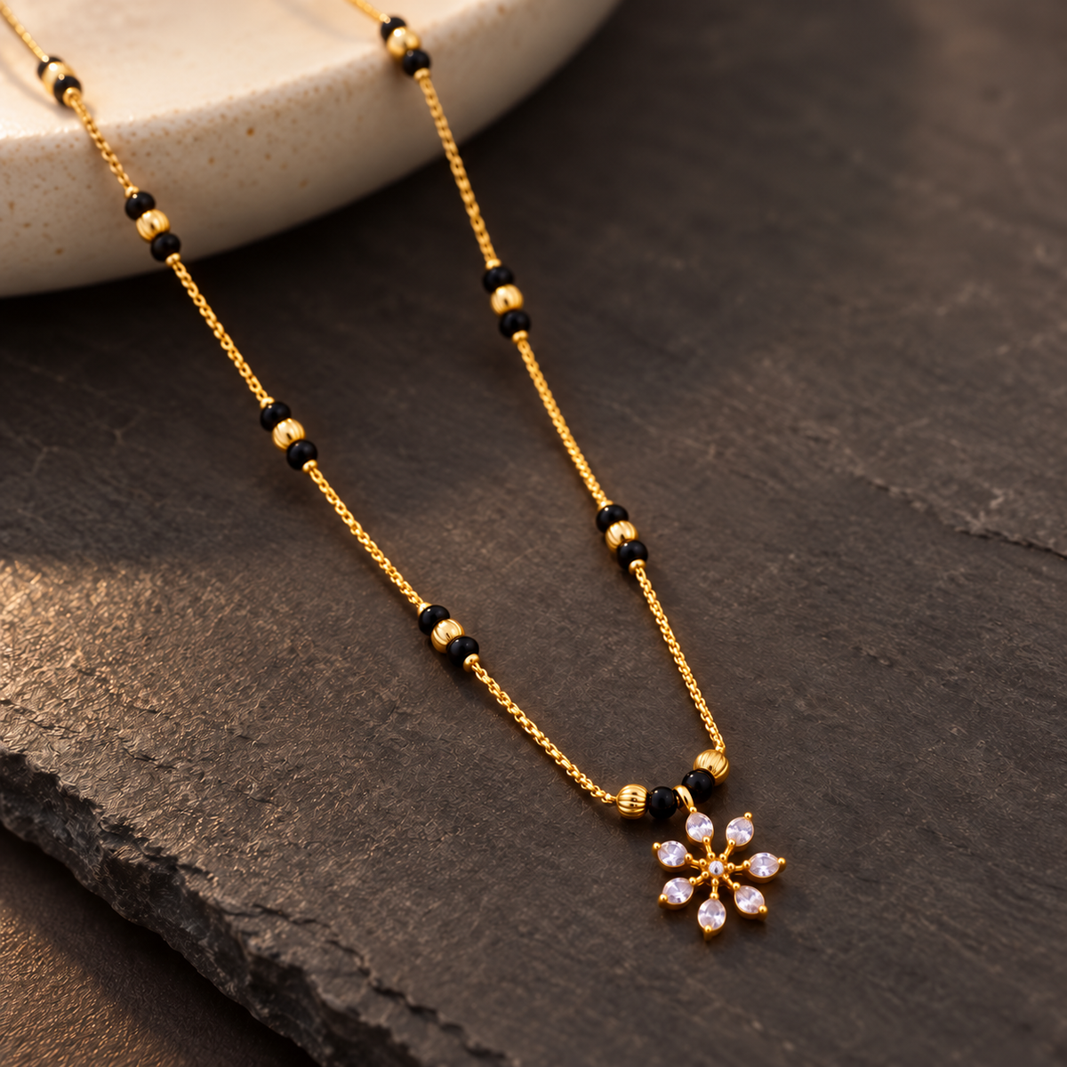 Angled view of Kairavi floral Mangalsutra on dark slate with cream ceramic