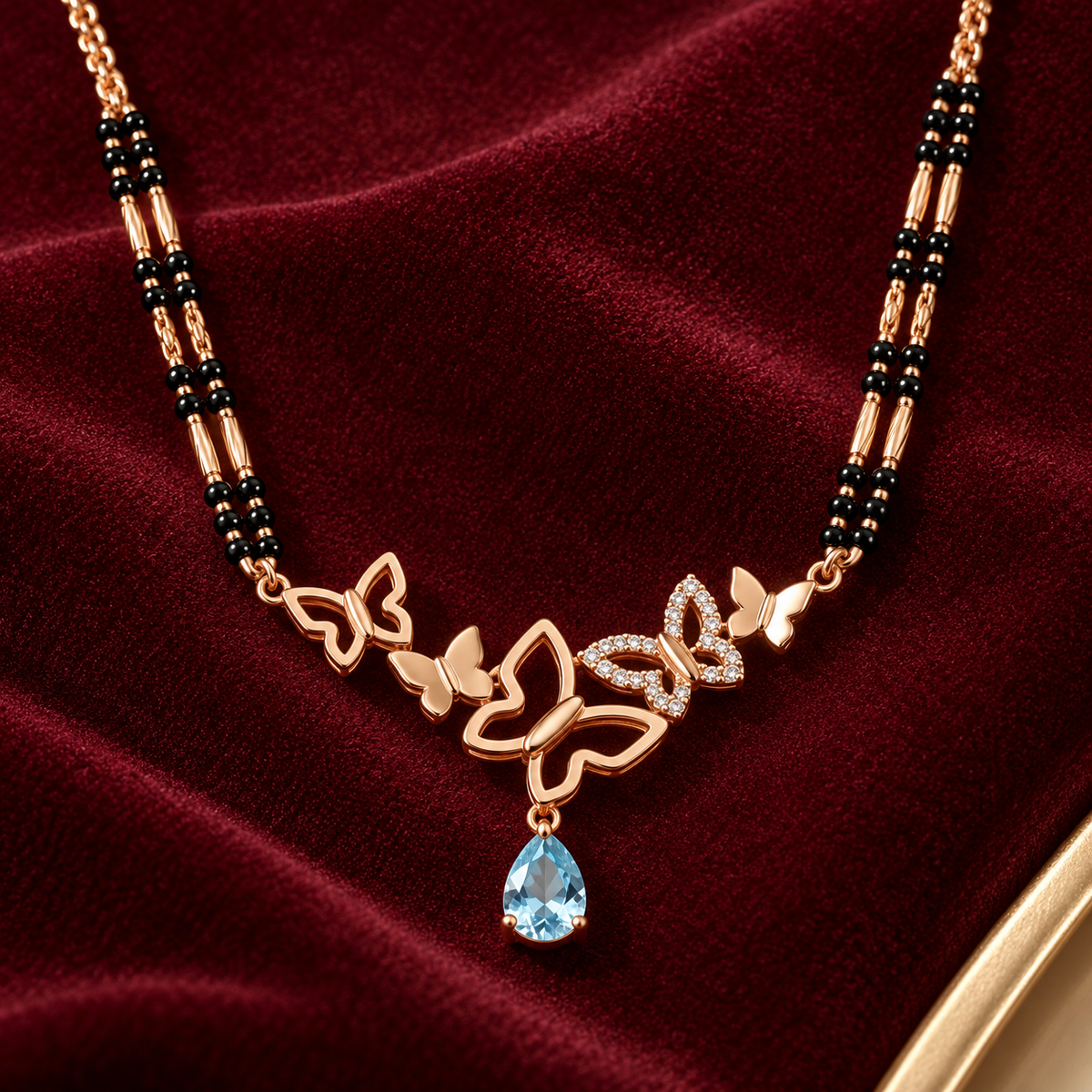 Close view of Mariposa butterfly pendant and pale blue pear drop on burgundy velvet.